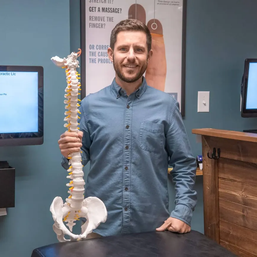 Chiropractor Dr. Evan Norum of Advantage Chiropractic holding a model of a skeletal spine.